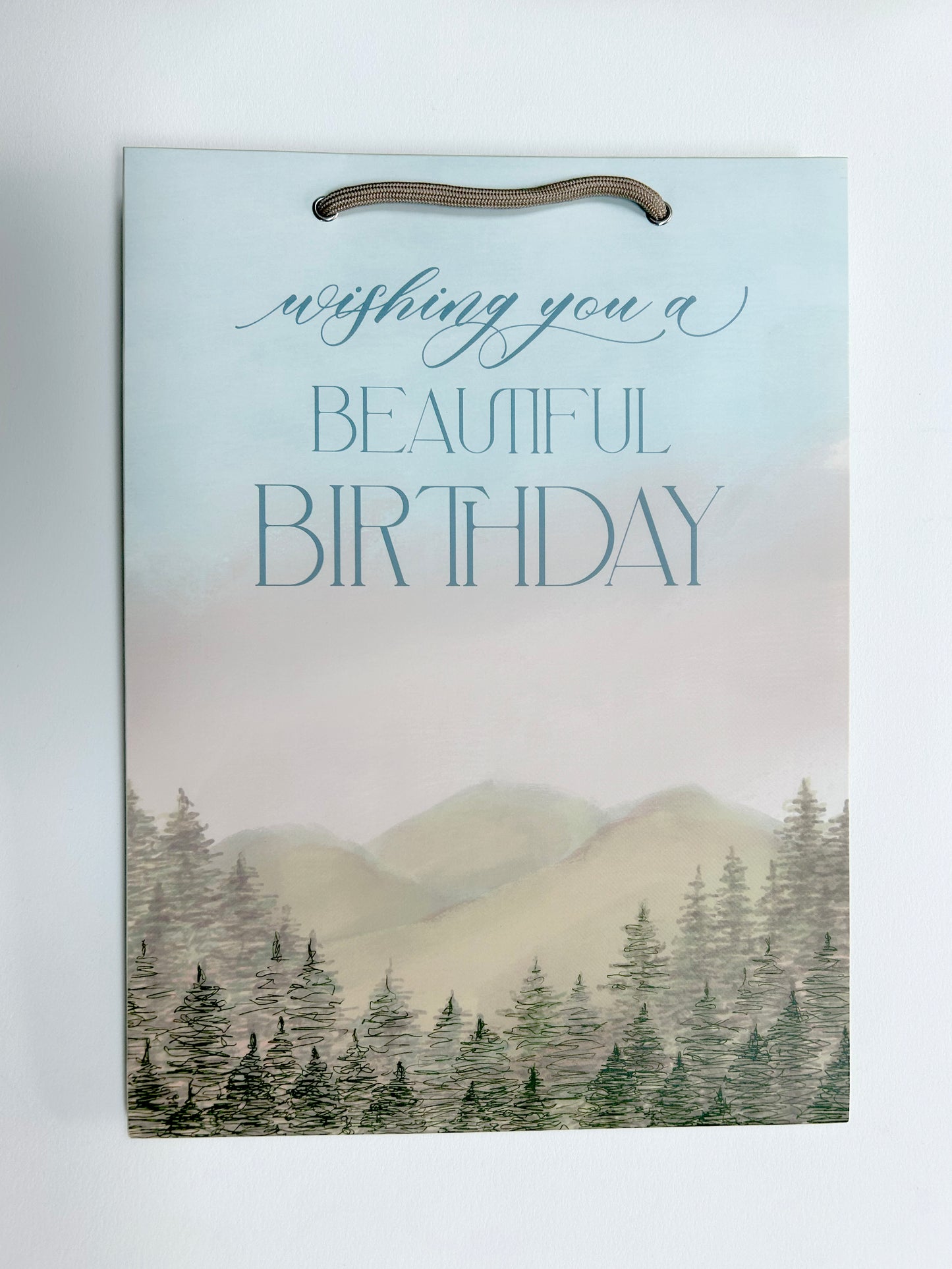 Flatlay photo of Rust Belt Love's birthday bag with mountain and tree illustrations that reads "Wishing you a beautiful birthday"