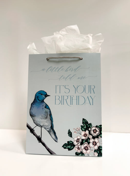 Standing up photo of blue gift bag with florals that reads "A little bird told me it's your birthday" by Rust Belt Love