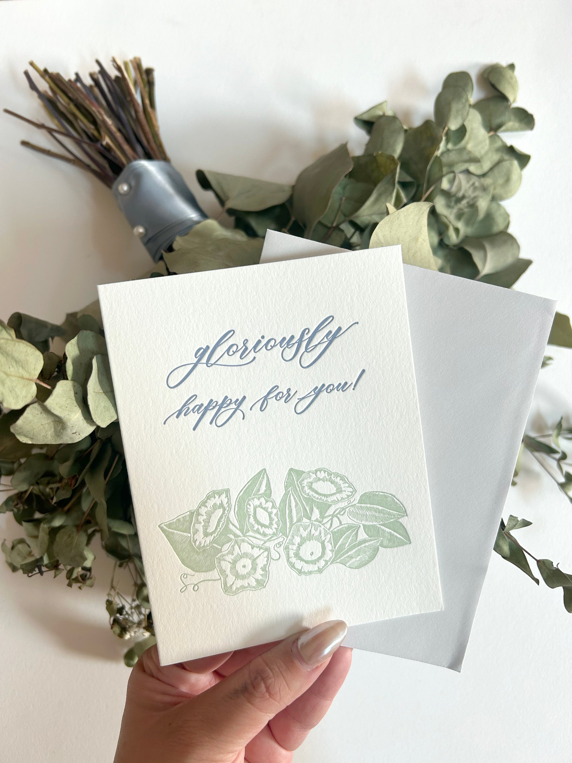 A style shot of Rust Belt Love's floral letterpress congrats cards that reads "gloriously happy for you!"