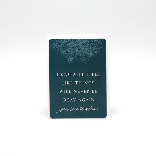 Dark teal floral minicard that reads "i now it feels like things will never be okay again you're not alone" by Rust Belt Love